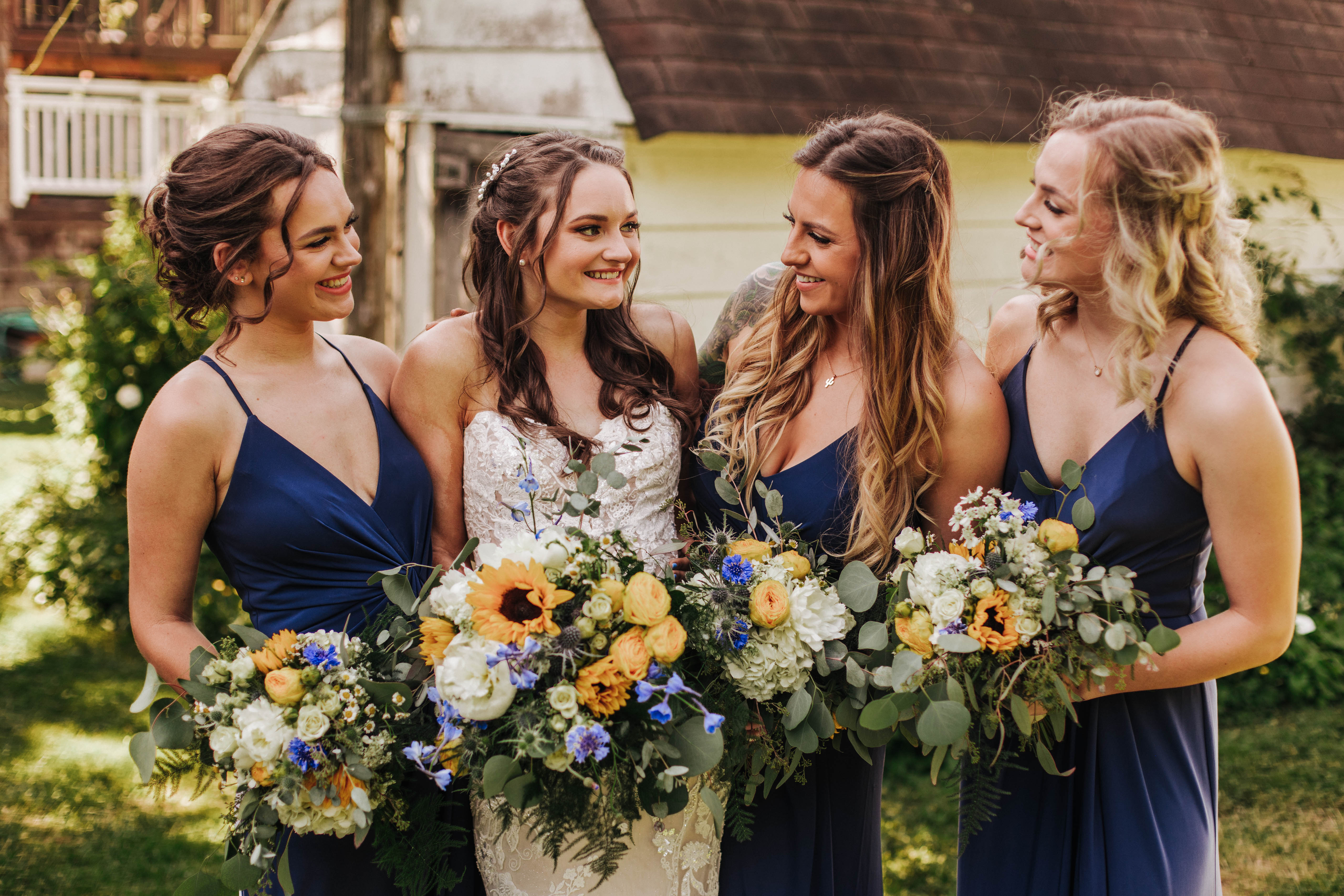 Bride and three bridesmaids smiling towards each other. On-location wedding hairstyles by Elle Marie Hair Studio.